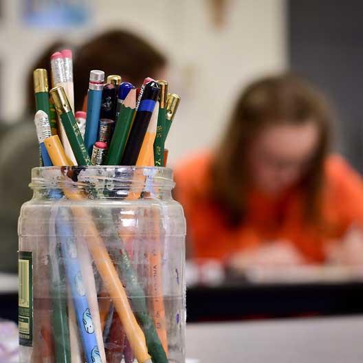 A jar of pencils, with a students at work in the background